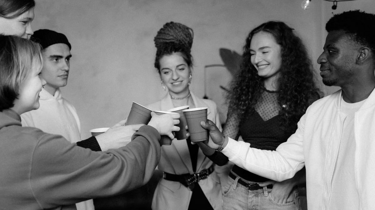 A diverse group of friends celebrates indoors, toasting with drinks and smiling.