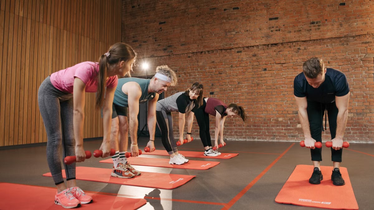 Fitness group performing exercises with dumbbells in a modern yoga studio setting.