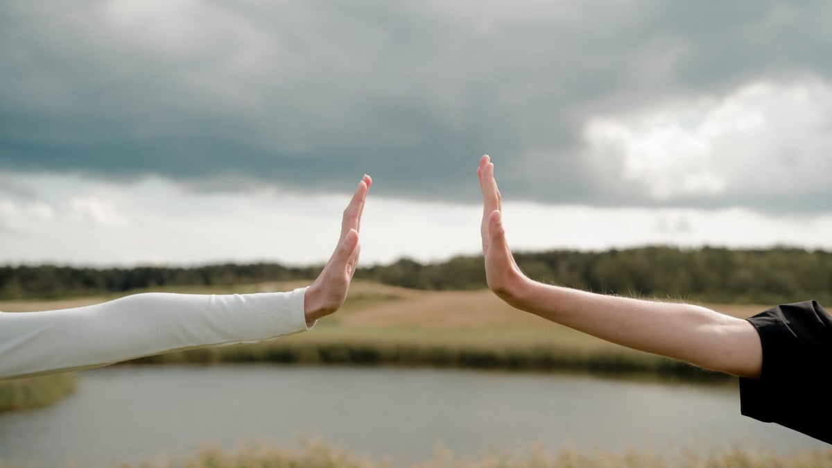 Two arms reaching out for a high five, symbolizing connection and distance in a natural setting.
